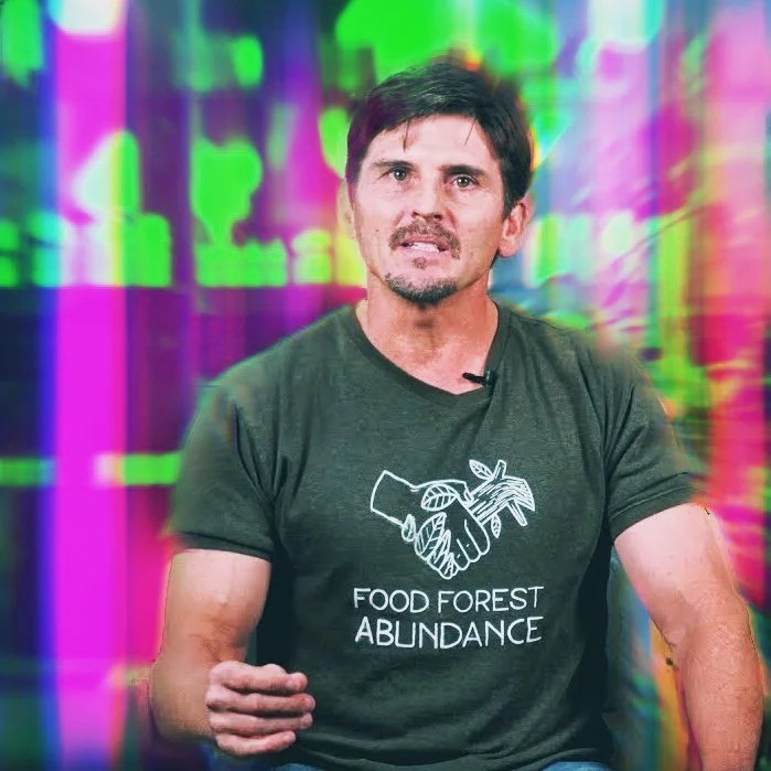 A vibrant video still of founder Jim Gale speaking to camera in a Food Forest Abundance shirt against a luminous, digital backdrop